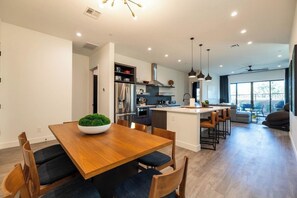 Une cuisine moderne dotée d’un îlot central, d’un coin repas avec une table et des chaises en bois, et offrant une vue sur l’extérieur grâce à de grandes fenêtres.