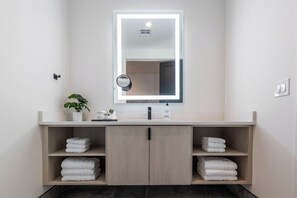 Une salle de bain moderne avec un grand miroir, deux porte-serviettes et une plante en pot.