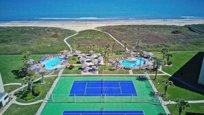 Ein Resort mit zwei Schwimmbecken, Tennisplätzen und Blick auf den Strand.