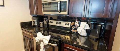 A compact kitchen with a microwave, stove, coffee maker, and a small dining area.