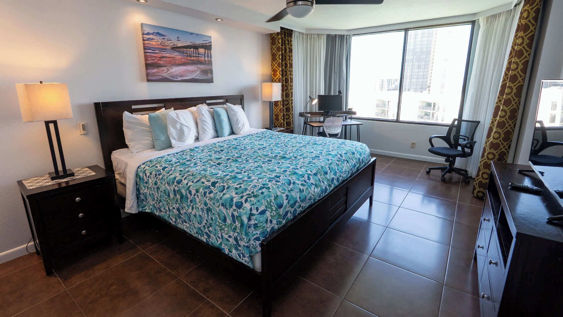 A hotel room with a bed, a desk, a chair, a TV, and a window with curtains.