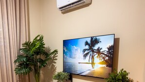 Olohuone, jossa on televisio, puinen kaappi, kaksi jakkaraa ja ruukkukasveja.