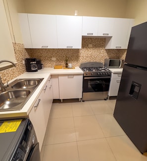A compact kitchen with white cabinets, a gas stove, a microwave, and a refrigerator. - Milyleo Home, Your Caribbean Hideaway – Private Jacuzzi & Tropical Comfort (Punta Cana)