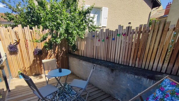 A wooden deck with a table and chairs, a small round table, and a colorful chair. - Le Carpe Diem Apartment, in Langeac, in the heart of the Allier Gorges (Langeac)