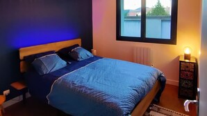 A bedroom with a bed, a window, a wall-mounted lamp, and a radiator. - Le Carpe Diem Apartment, in Langeac, in the heart of the Allier Gorges (Langeac)