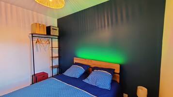 Una habitación con cama, lámpara colgante, estante con cajas y pared verde.