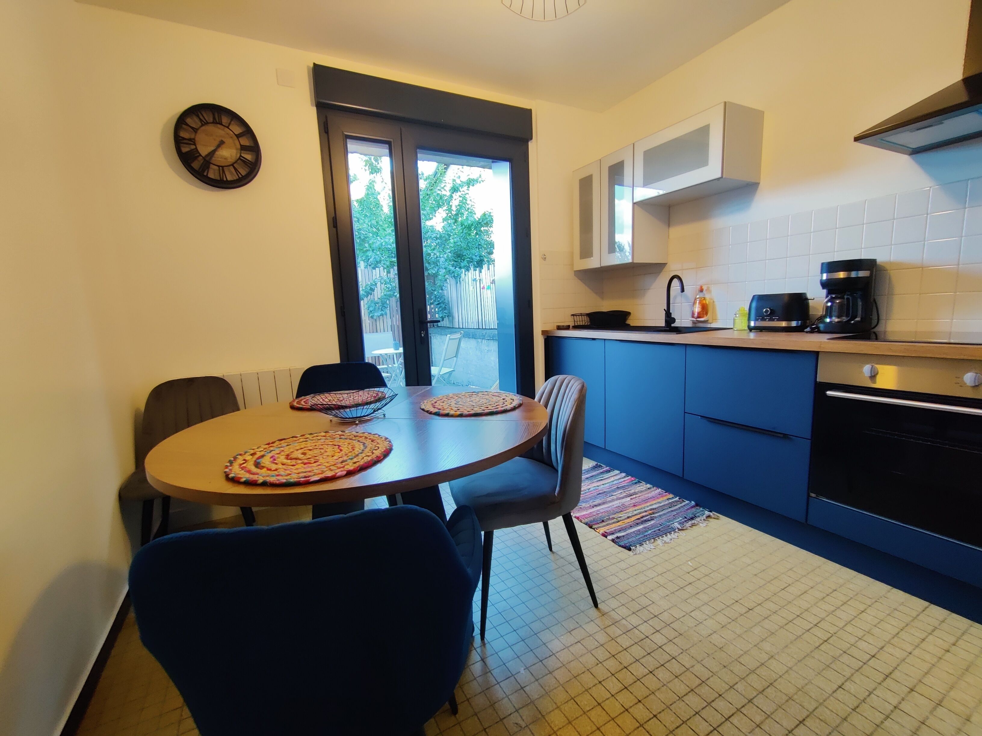 Cocina compacta con zona de comedor, que incluye una mesa redonda con sillas, un reloj y vistas a través de la puerta.