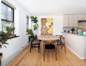 A modern kitchen with a dining area, wooden flooring, and potted plants.
