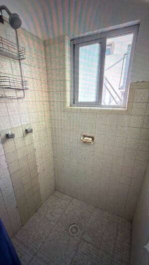 Un piccolo bagno rivestito di piastrelle, con finestra, soffione e scarico.