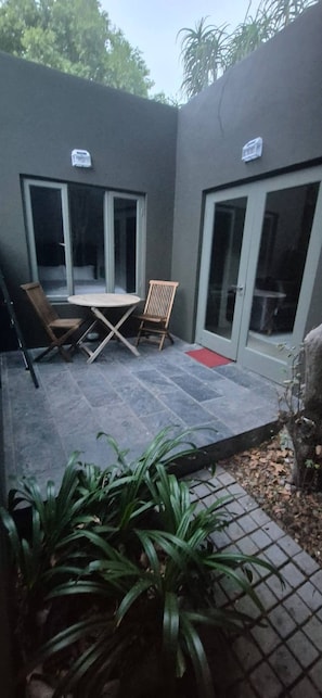 A patio with a table and chairs, a sliding glass door, and a small red mat. - Cozy 2 Bedroom Cottage (Johannesburg)