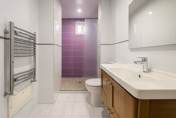 Un baño moderno con lavamanos blanco, grifo cromado y ducha con toallero de cromo.
