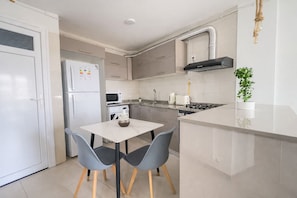 Una cocina moderna con refrigerador blanco, microondas, estufa y pileta. Hay una pequeña mesa de comedor con dos sillas.