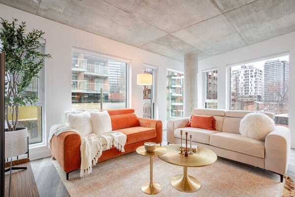 Ein modernes Wohnzimmer mit zwei Sofas, einem Couchtisch und einem großen Fenster mit Blick auf die Stadt.