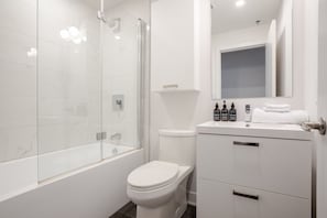 A modern bathroom with a glass-enclosed shower, a toilet, and a vanity with toiletries. - Stylish MTL Apartment | Parking + EV Charger (Montreal)