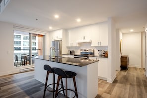 Eine moderne Küche mit einer zentralen Kochinsel, Edelstahlgeräten und Blick auf einen Außenbalkon.