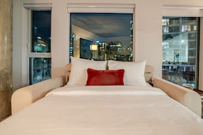 A hotel room with a large bed, a city view through the window, and a glass door leading to an outdoor area. - Stylish MTL Apartment | Parking + EV Charger (Montreal)