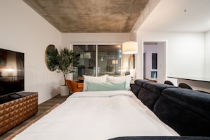 Ein modernes Hotelzimmer mit einem großen Bett, einer Couch, einem Fernseher und einem Essbereich mit Tisch und Stühlen.