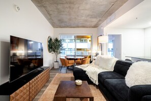 Ein modernes Wohnzimmer mit Flachbildfernseher, einer Couch, einem Couchtisch und einem Essbereich mit Stühlen und Tisch.