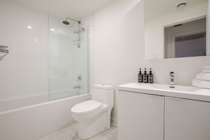 Ein modernes Badezimmer mit einer gläsernen Dusche, einer weißen Toilette und einem Waschtisch mit Pflegeprodukten.