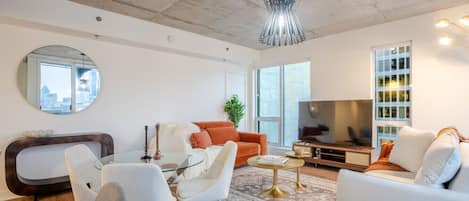 Una sala moderna con una mesa de centro de vidrio, sofás blancos, un televisor y vistas a la ciudad.