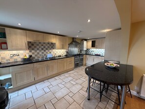 A modern kitchen with a central island, stainless steel appliances, and a tiled backsplash. - Lymington Seaside Cottage Retreat (Lymington)