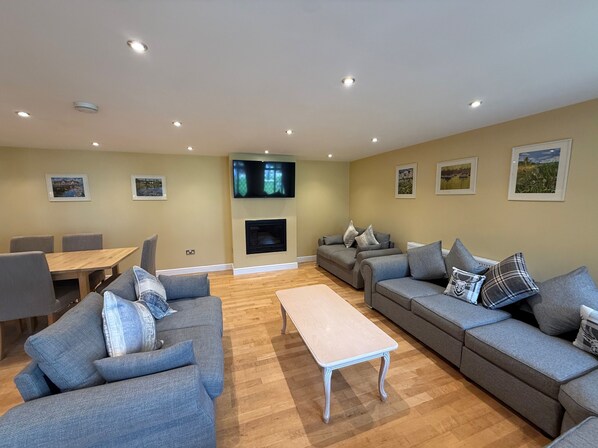 A living room with a sofa set, a coffee table, a TV mounted above a fireplace, and framed pictures on the walls. - Lymington Seaside Cottage Retreat (Lymington)