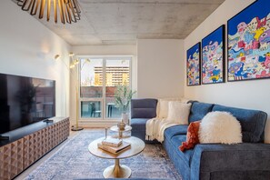 A modern living room with a flat-screen TV, a sofa, a coffee table, and a large window. - Urban Oasis Downtown with Parking (Montreal)