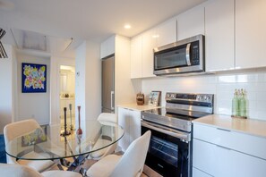 A modern kitchen with stainless steel appliances, a glass dining table, and white cabinetry. - Urban Oasis Downtown with Parking (Montreal)