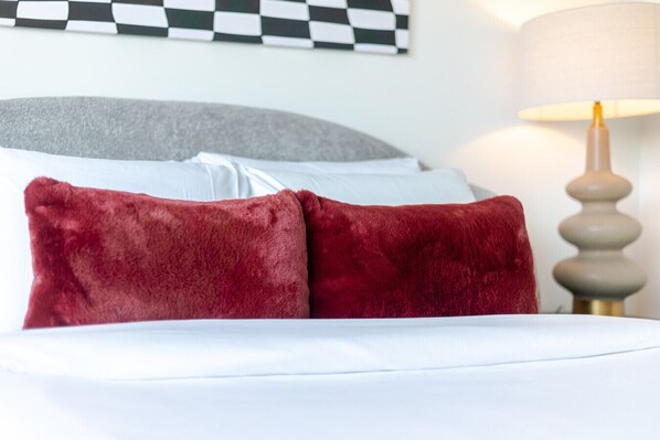 A bed with white bedding and two red pillows, a grey headboard, and a lamp with a white lampshade. - Urban Oasis Downtown with Parking (Montreal)