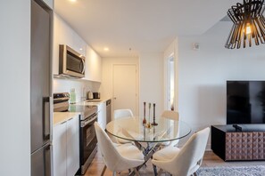 Une cuisine moderne avec une table à manger en verre, des chaises blanches, un téléviseur et un luminaire au plafond original.