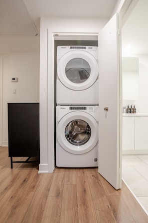 A laundry room with two stacked Whirlpool front-loading washing machines, a black cabinet, and a white door. - Urban Oasis with Parking (Montreal)
