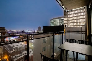 En balkon med et bord og stole, der vender ud mod et bybillede med bygninger og en bro.