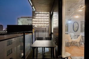 Et moderne interiør med et spiseområde, et fjernsyn på en balkon og udsigt til bygningerne.