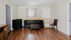 Ein Zimmer mit einer schwarzen Couch, einem kleinen Holztisch, einem Korbstuhl und einer weißen Tür.
