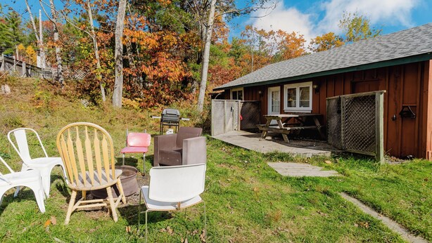 Ein rustikales Blockhaus mit Terrasse, Sitzgelegenheit im Freien und Blick auf Herbstbäume.