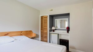 Ein Schlafzimmer mit einem Bett, einem Holz-Kopfteil, einem Schreibtisch mit Spiegel und einer kleinen Kommode.