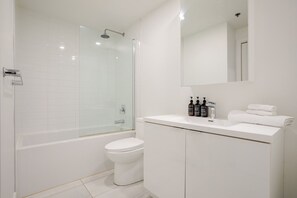 Une salle de bain moderne avec une douche à parois de verre, des toilettes blanches et un meuble-lavabo avec des articles de toilette.