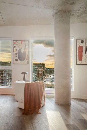 Une pièce moderne avec une grande fenêtre, une chaise blanche et des œuvres d’art abstraites accrochées aux murs.