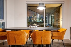 Un comedor con una mesa grande, seis sillas, una lámpara colgante moderna y vistas a la ciudad a través de amplios ventanales.