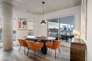 Un espace de restauration moderne avec une table ronde, des chaises orange et une vue sur la ville à travers de grandes fenêtres.