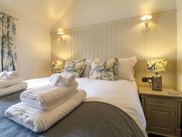 A neatly made bed with floral pillows, a bedside lamp, and a folded towel on the nightstand. - Hope Cottage (Bakewell)