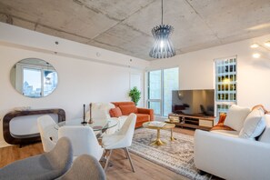 Ein modernes Wohnzimmer mit einem Glastisch, weißen Sofas, einem Fernseher und Blick auf die Stadt.