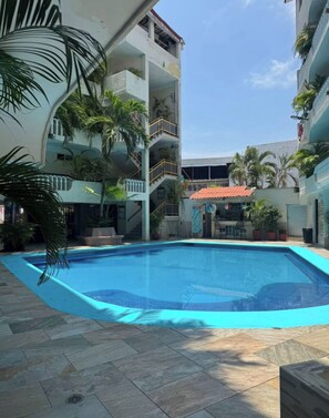 A swimming pool surrounded by tiled flooring, with a multi-level building in the background. - Boutique Diana (Acapulco)