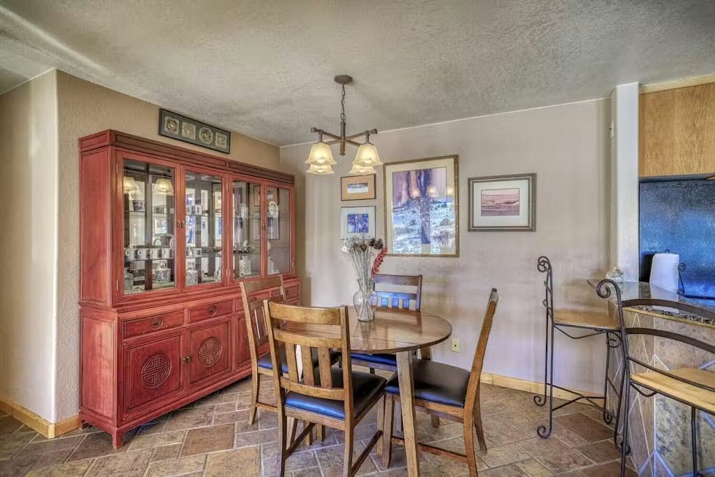 A dining area with a wooden table and chairs, a red cabinet with glass doors, and a hanging light fixture.