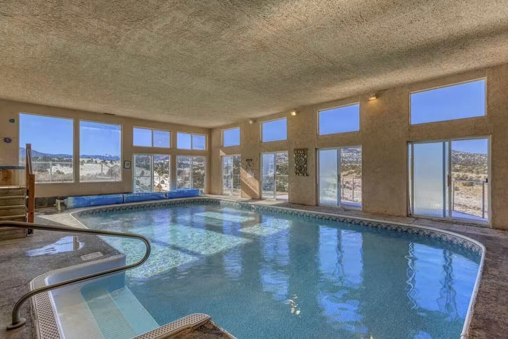 An indoor swimming pool with a view of a desert landscape through large windows.