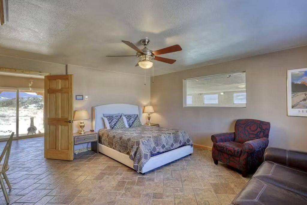 A bedroom with a bed, a ceiling fan, a chair, and a window.