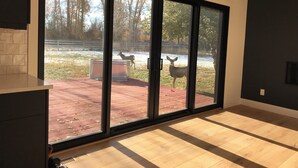 A room with a large sliding glass door leading to an outdoor area with a deer and a fenced enclosure.