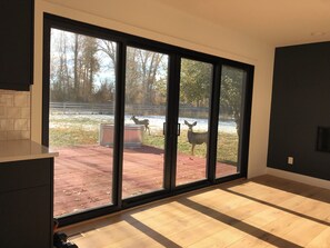 A room with a large sliding glass door leading to an outdoor area with a deer and a fenced enclosure.