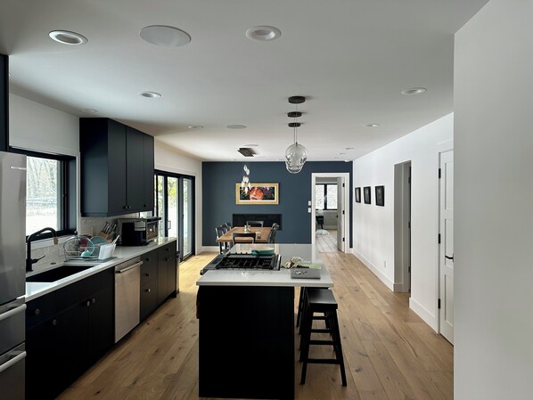 Une cuisine moderne dotée d’un îlot central, de meubles de rangement aux couleurs sombres et d’un éclairage encastré.