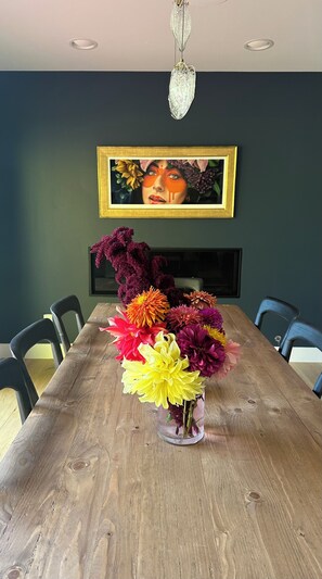 Ein Esstisch mit floraler Dekoration, ein gerahmtes Kunstwerk an der Wand und eine Chandelier darüber.
